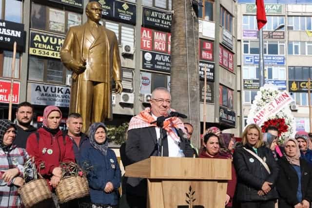 Kadın ve erkekler, etkinlikte lideri dinlerken, kent meydanında politika ve halk iletişimini vurguluyor.