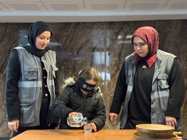 Çalışanlar ve öğrenci, basın merkezinde su doldurma ve bilgi alışverişi yapıyor.